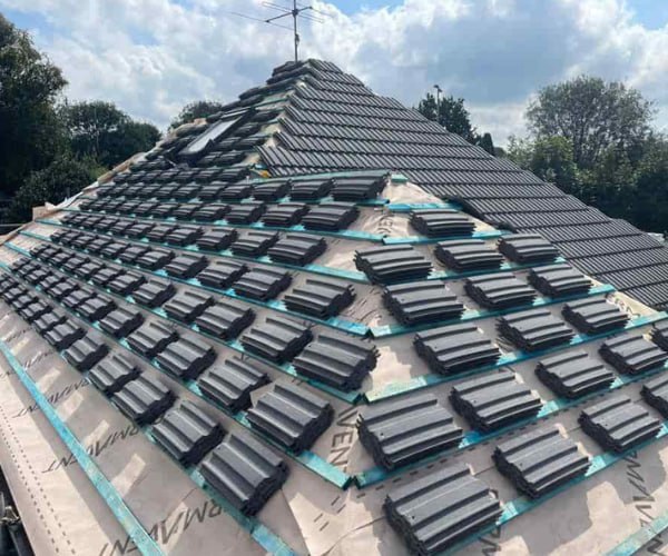 This is a photo of a new hip roof being installed. New felt, battens, and grey tiles have been installed, also a new velux window. Works carried out by EA Roofing Daventry