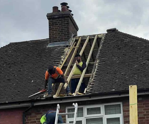 This is a photo of a roof repair being carried out. A section of the roof has been stripped and two roofers are replacing the rafters. Works being carried out by EA Roofing Daventry